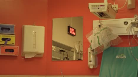Hospital-mirror-with-a-clock-reflection-on-an-orange-wall-with-tissues-and-baby-equipment