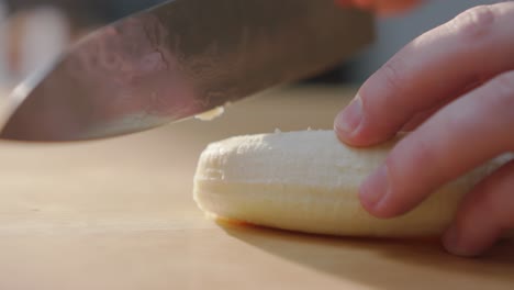 Hand-Cutting-a-Banana-on-a-Wooden-Surface