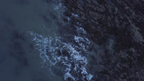 4K-drone-shot-of-waves-on-a-rocky-winter-shore,-from-a-top-down-angle