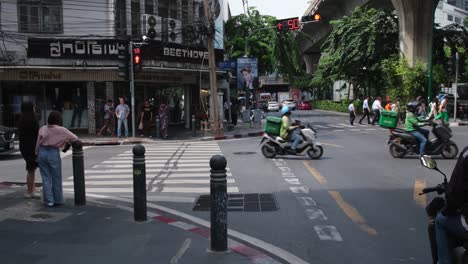 People-waiting-to-cross-the-street-as-a-red-sports-car-passes-by-followed-by-Grab-Motorcycle-delivery,-Sukhumvit-26-in-Bangkok,-Pedestrian-Lane,-Thailand
