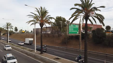 Mediterranean-Highway-Panoramic,-Cars-Driving-Along-Beach-Side-Barcelona-Spain-with-Palm-Trees-Waving-with-the-Wind