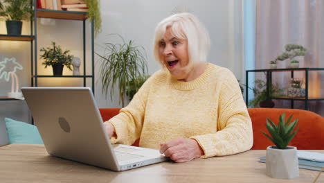Overjoyed-senior-woman-working-on-laptop-celebrate-success-win-money-in-lottery-get-online-good-news