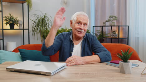 Senior-man-smiling-friendly-at-camera,-waving-hands-gesturing-hello,-hi,-greeting-at-home-on-couch