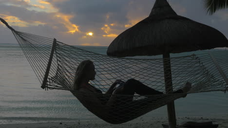 Woman-relaxing-in-hammock-on-beach-and-taking-cell-photos