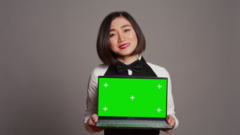 Asian-server-presenting-greenscreen-display-on-laptop-in-studio