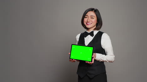 Asian-receptionist-holding-tablet-with-greenscreen-on-camera,