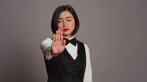Asian-administrator-showing-stop-sign-with-palm-raised-in-studio,