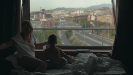 Blick-Auf-Die-Auf-Dem-Bett-Liegende-Mutter-Mit-Ihrem-Kleinen-Sohn-Vor-Einem-Riesigen-Panoramafenster-Und-Dem-Stadtbild-Von-Barcelona,-Spanien