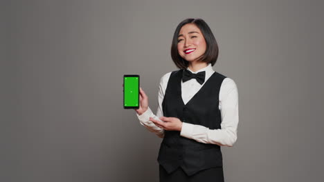 Asian-hotel-concierge-pointing-at-phone-with-greenscreen-layout