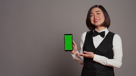 Asian-hotel-concierge-pointing-at-phone-with-greenscreen-layout