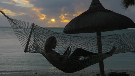 Woman-with-phone-lying-in-hammock-on-the-beach