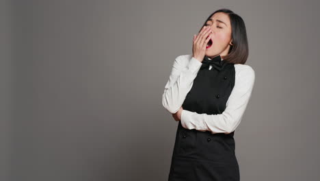 Exhausted-waitress-with-apron-yawning-over-grey-background
