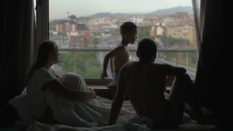 Blick-Auf-Die-Familie-Auf-Dem-Bett-Mit-Kleinem-Sohn-Vor-Riesigem-Panoramafenster-Und-Stadtbild-Von-Barcelona,-Spanien