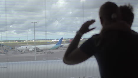 Back-view-of-mother-and-son-standing-and-watching-in-the-window-on-the-airplane-runway-Amsterdam-Netherlands