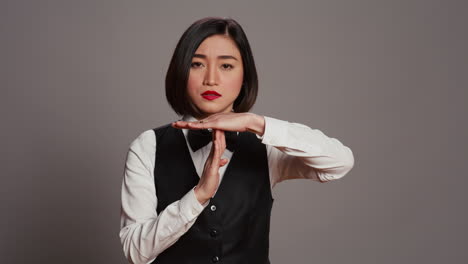Asian-receptionist-expressing-timeout-symbol-on-camera