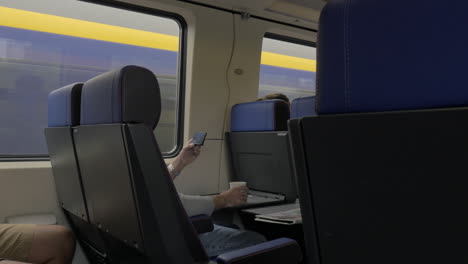 View-of-men-in-the-train-and-working-with-laptop-on-the-table-and-drinking-against-window-Netherlands