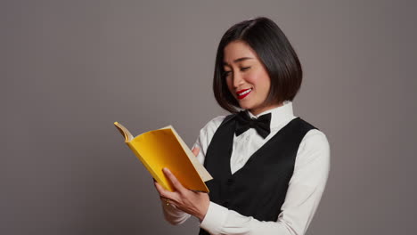 Asian-receptionist-reading-a-literature-book-over-grey-background