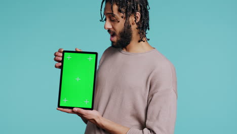 Man-holds-green-screen-tablet,-showing-positive-emotion,-studio-background