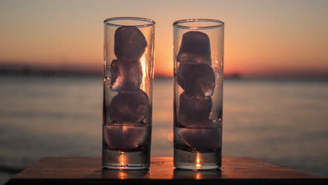 Glasses-with-melting-ice-against-sea-and-sunset-background