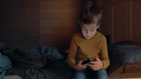 Child-with-cellphone-sitting-on-bed-at-home
