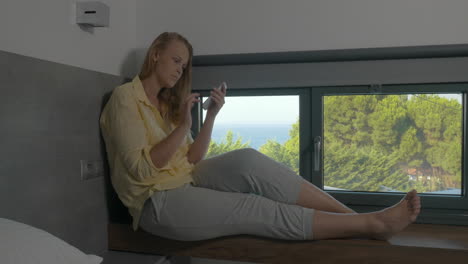 Woman-sitting-on-window-sill-and-using-phone