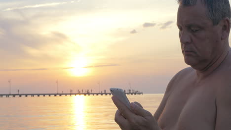 Man-with-Smartphone-by-the-Sea-at-Sunset