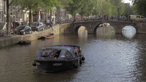 Blick-Von-Der-Brücke-Auf-Das-Sich-Auf-Dem-Kanal-Bewegende-Boot-Mit-Menschen-In-Amsterdam,-Niederlande