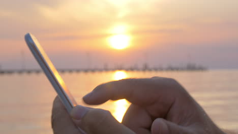 Man-typing-on-smartphone-by-sea-at-sunset