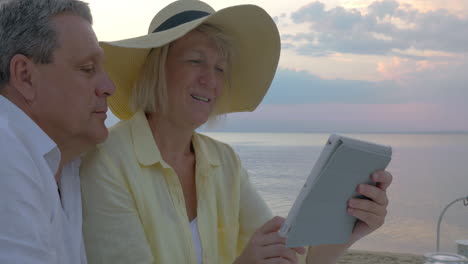 Senior-couple-using-touch-pad-at-the-seaside