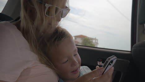 Mother-and-son-using-mobile-phone-during-car-ride