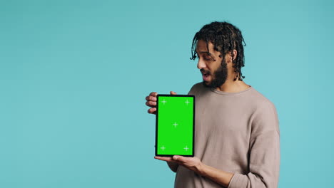 Man-holding-green-screen-tablet,-showing-positive-emotion,-studio-background