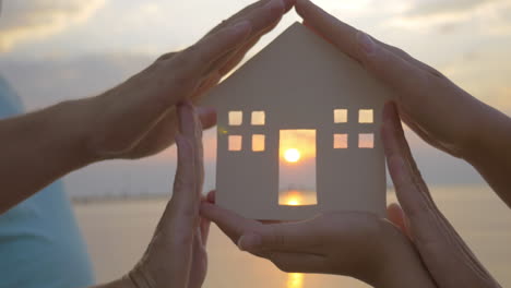 Hands-Holding-House-Silhouette-against-Sun