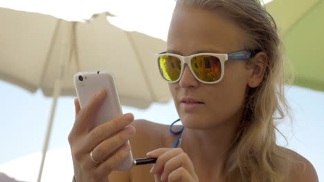 Frau-Mit-Sonnenbrille-Benutzt-Handy-Am-Strand