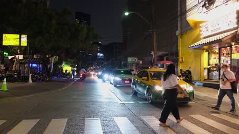 People-crossing-a-pedestrian-lane-in-a-busy-corner-street-near-Asok-and-Petchaburi-intersection-where-vehicles-are-taking-turns-in-making-a-left-turn-towards-Ratchadaphisek-in-Bangkok