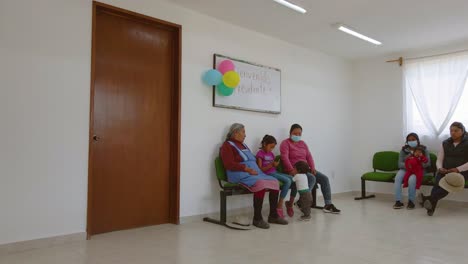 Several-women-wearing-masks-and-children-are-waiting-outside-of-a-beautiful-clinic-adorned-with-colorful-balloons-in-Ecatepec-de-Morelos,-Mexico