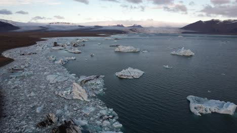 Panorama-aerial-orbit-ice-floes-in-lake-with-glacier-in-Jokulsarlon,-Iceland
