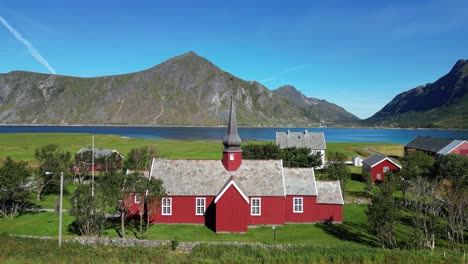 Red-wooden-church-in-Flakstad,-Lofoten-Islands,-Norway,-Scandinavia---Aerial-Backwards