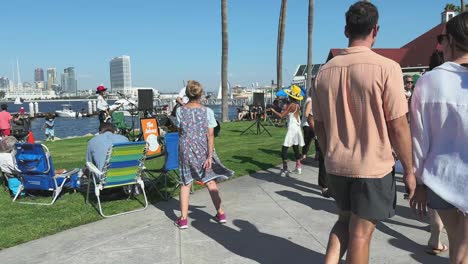 Coronado-island-and-people-dancing-tougher-on-the-walkway,-all-generations,-with-Downtown-San-Diego-in-the-background