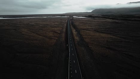 Epic-flying-over-empty-road-in-mossy-volcanic-stone-nature,-epic-moody-dark-landscape-distant-view-iceland