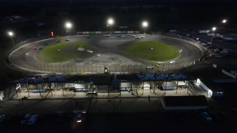 Cars-speeding-around-track-at-night,-aerial-view