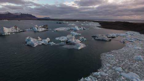 Sunset-glacial-lake-Jokulsarlon-in-iceland,-cinematic-aerial-over-melting-ice