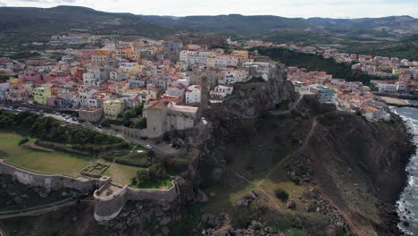 city-of-Castelsardo,-Sardinia:-aerial-view-travelling-out-over-the-colorful-city-and-its-historic-tower-on-the-island-of-Sardinia