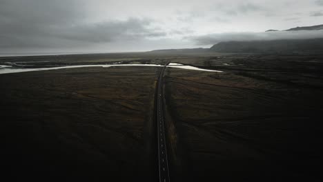 Cinematic-aerial-car-driving-on-ring-road-in-mossy-volcanic-stone-nature,-moody-dark-landscape-view-iceland