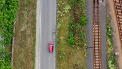 A-red-car-driving-on-an-asphalt-road-next-to-a-railway
