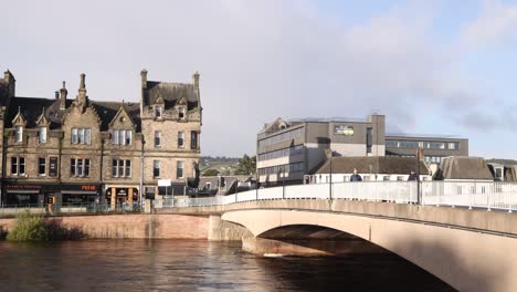 panning-shot-of-storefront-and-townhomes-and-bridge-in-Inverness,-Scotland-in-the-Highlands