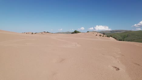 Aerial-dolly-tilt-up-above-epic-dunes-with-foot-steps-in-golden-sand