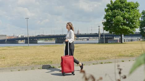 Young-entrepreneur-female-travel-to-new-city-with-red-luggage,-follow-view