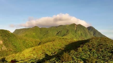 Aerial-approaching-shot-of-green-covered-mountains-on-Orchid-Island-蘭嶼-during-golden-hour-in-Taiwan,-Asia---White-Clouds-behind-summit-at-blue-sky
