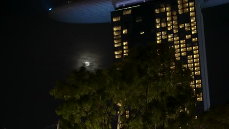 Moon-Shining-Through-Night-Time-Clouds-Behind-Tower-Of-Marina-Bay-Sands-Hotel-In-Singapore
