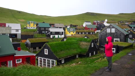 Female-hiker-enjoys-the-view-of-greenish-Mykines-village-with-colorful-houses,-Faroes